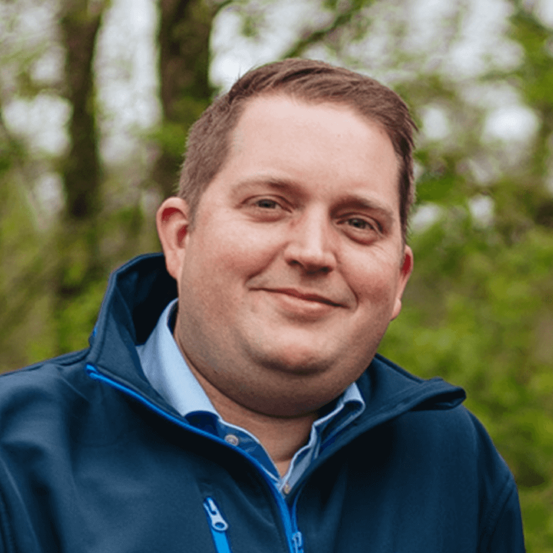 Killian wearing a dark blue jacket. Killian is looking happy directly into the camera. He is wearing black-framed eyeglasses.
