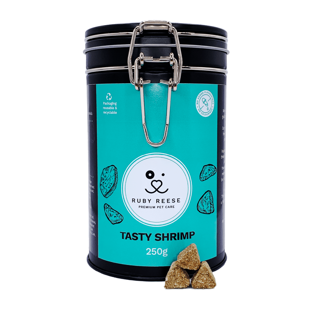 A black tin of RUBY REESE TASTY SHRIMP natural dog treats with an turquoise label with some treats spilled in front of it